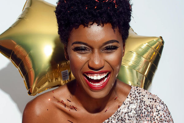 woman standing in front of gold star balloons laughing wearing glam makeup