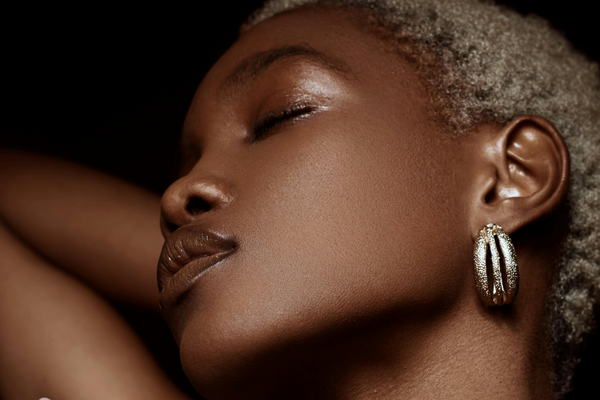 dark skinned model with short blonde hair with her eyes closed and wearing silver earrings