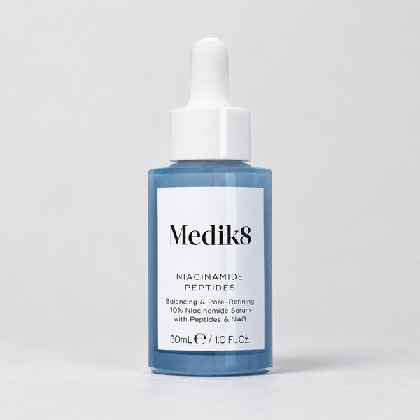 Medik8 Niacinamide Peptides Balancing & Pore-Refining Serum in a 30mL blue glass dropper bottle with a white label and white dropper cap, set against a light gray studio background.