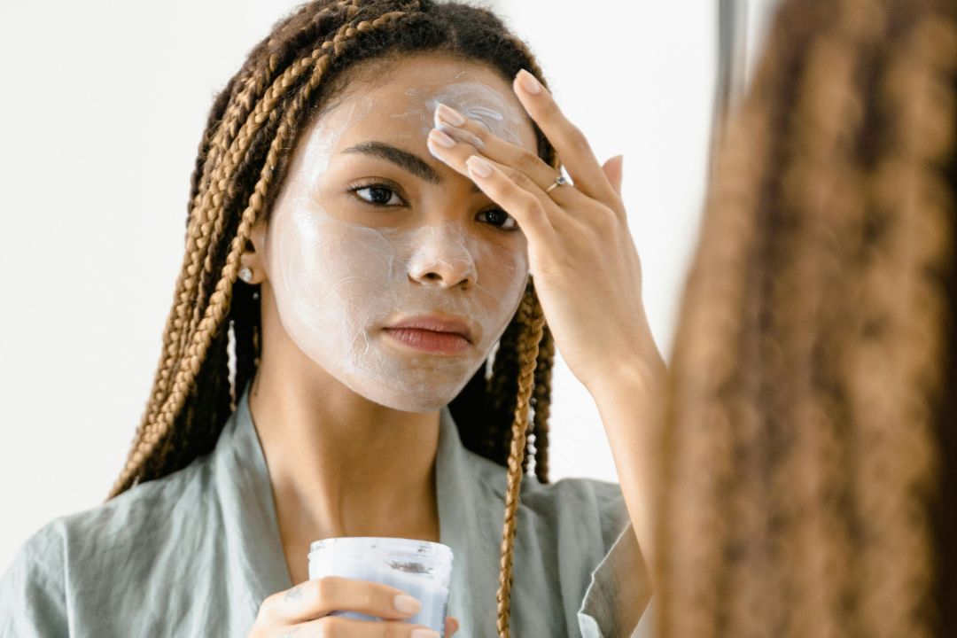 Girl applying face mask to her skin looking into a mirror