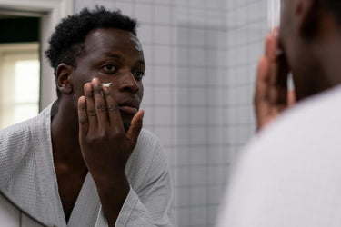 man looking in the mirror putting skincare onto his face