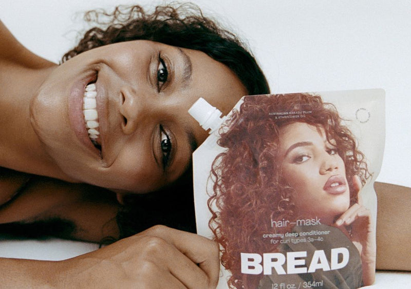 Smiling lady holding a pouch of BREAD Beauty Supply hair mask