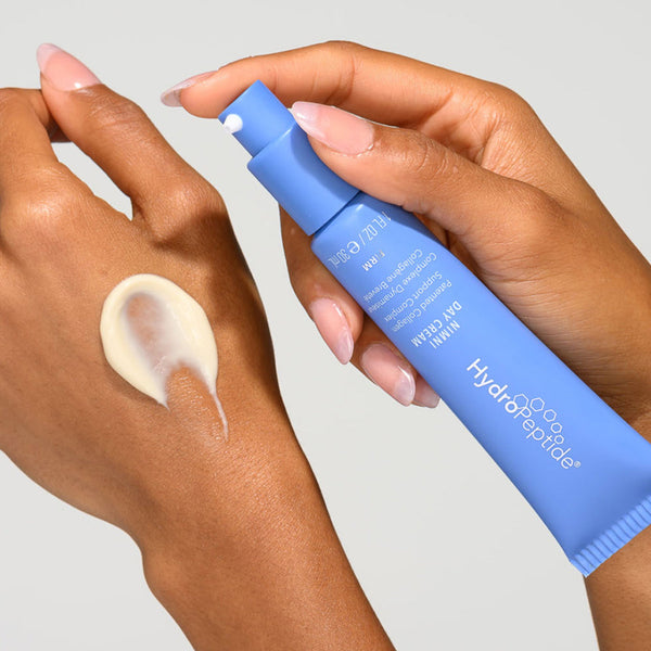 Hand applying cream from a blue bottle labeled 'Hydra Peptide' on a light gray background