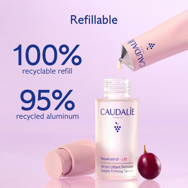 Caudalé Paris refillable serum bottle shown with a pink applicator tube being dispensed, a second tube lying on its side, and a small red fruit on a soft lavender background. Large text highlights recyclable refill and recycled aluminum.