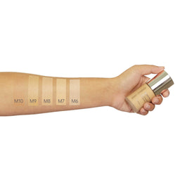 Hand holding a cosmetic product with color swatches on an arm