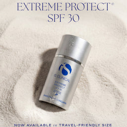 IS Clinical Extreme Protect SPF 30 sunscreen bottle in a silver travel-friendly size, set in a textured white sand-like background with promotional text overlays.