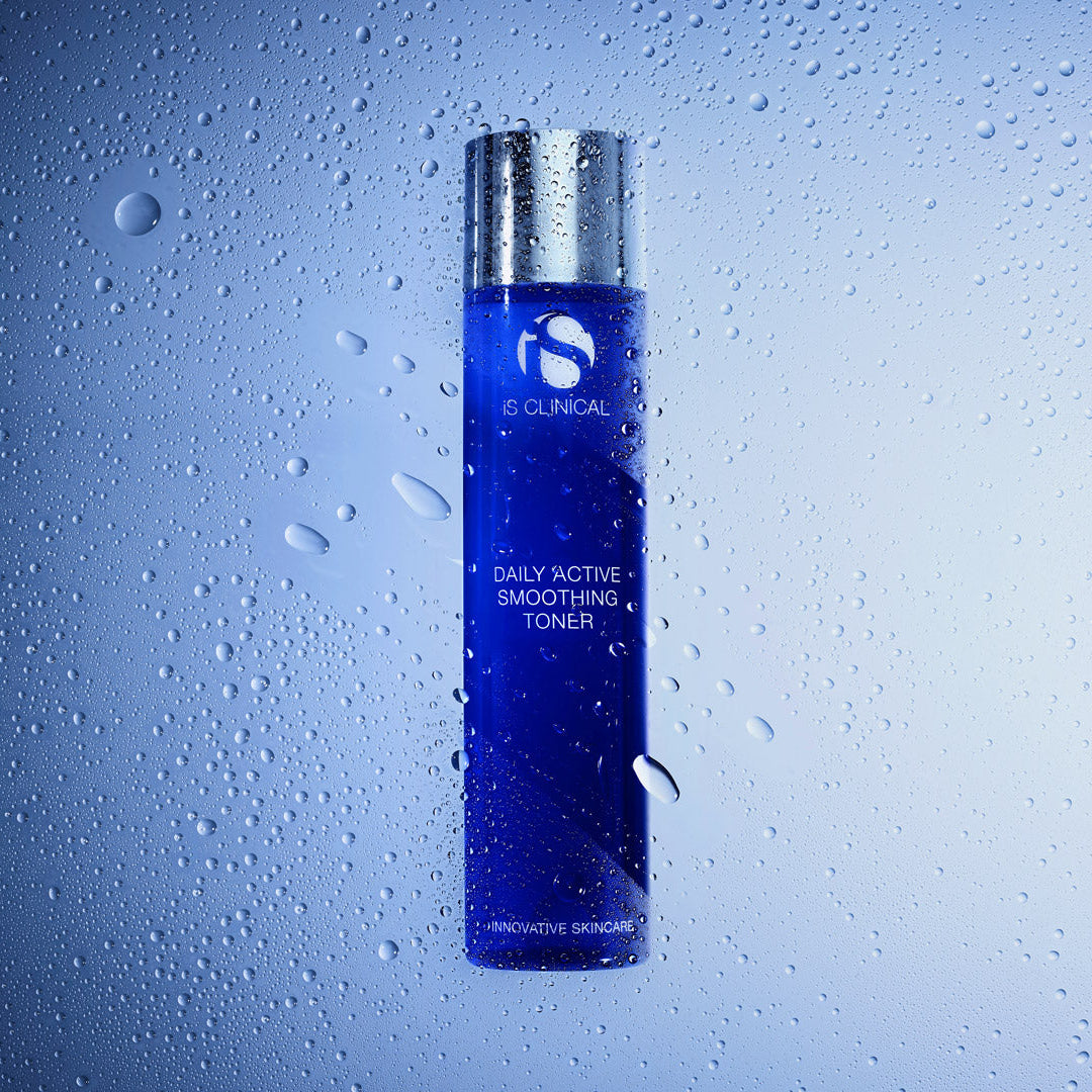 A bottle of e:CLINICAL Daily Active Smoothing Toner with a metallic silver cap and a deep blue body, shown against a cool blue gradient background with water droplets on a glass-like surface.