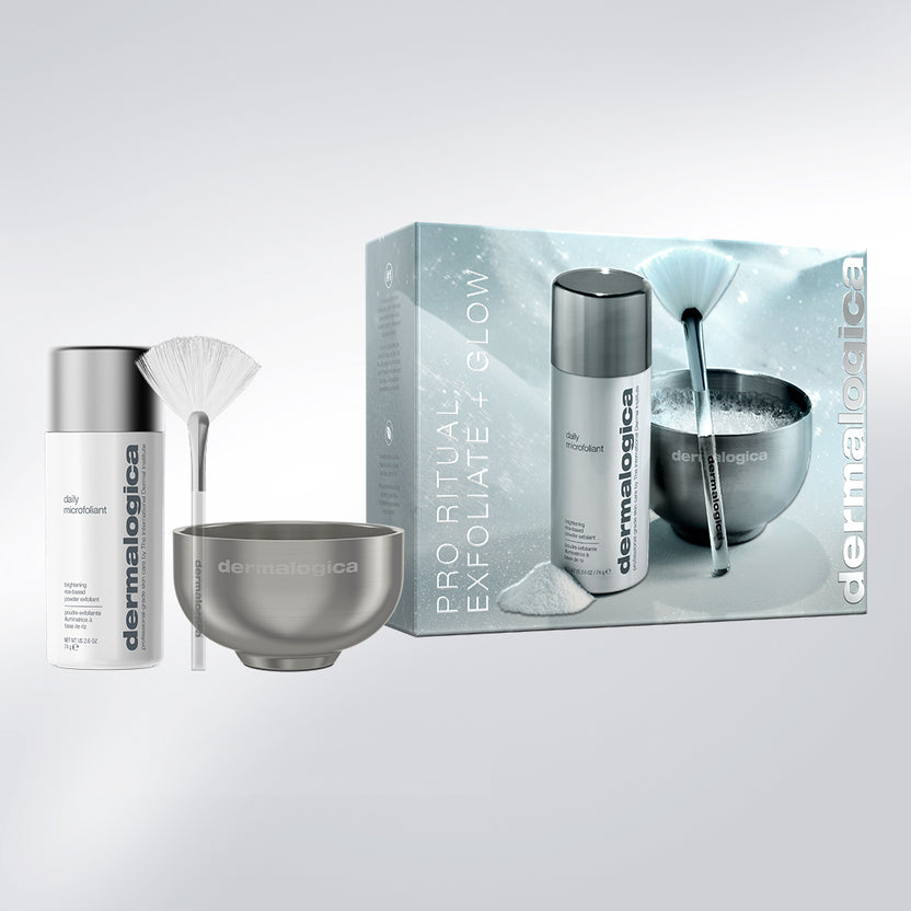 Dermalogica Pro Ritual Exfoliate + Glow gift set featuring a white and silver exfoliating bottle, a metallic bowl, a white fan brush, and the product packaging box on a light gray background.