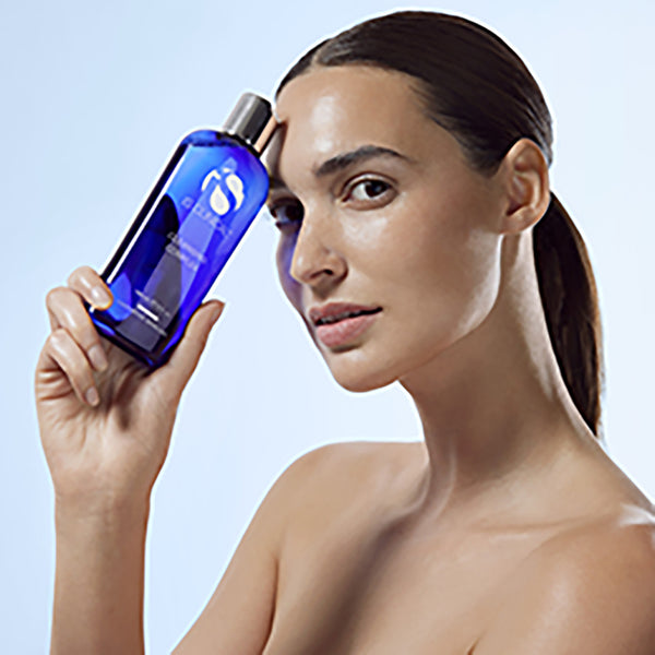 Woman holding a blue skincare bottle against a light blue background
