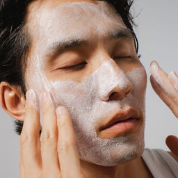 Person applying a facial mask to their face with a neutral background