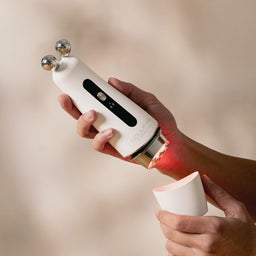 Hand holding a white handheld device with a red light on a beige background