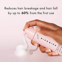 Hand holding a pink bottle of Hairgain scalp tonic with text on a light pink background