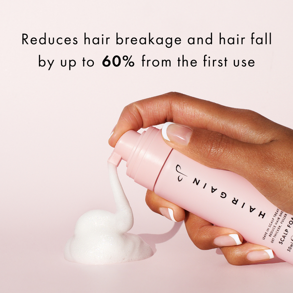 Hand holding a pink bottle of Hairgain scalp tonic with text on a light pink background