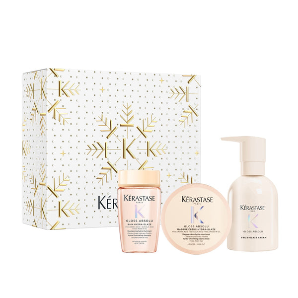 Kérastase Gloss Absolu hair care gift set featuring a white and gold patterned box, a pink bottle of gloss, a round jar of hair oil, and a pump bottle of leave-in conditioner, arranged on a white background.
