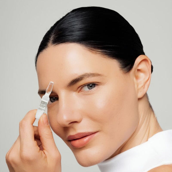 Woman holding a dropper with a clear liquid against a neutral background