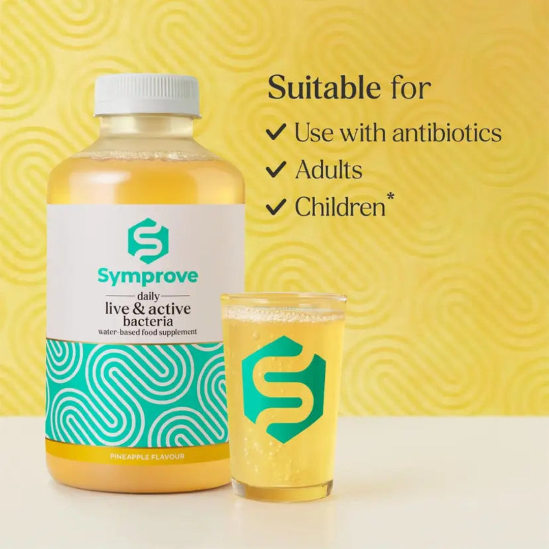 A bottle of Symprove daily live & active bacteria water based food supplement next to a glass of the yellow pineapple-flavoured liquid, set against a yellow patterned background with text stating 'Suitable for Use with antibiotics Adults Children'.