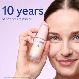 A woman holds a bottle of Caudalie Effacer Lines Visibles Retinol Night Repair Lotion against a light lavender background, with text reading '10 years of firmness restored'.