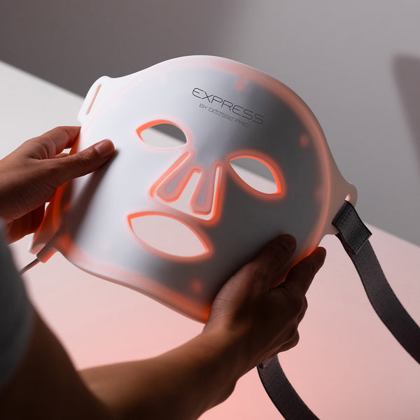 Person holding a LED face mask with glowing red accents on a neutral background