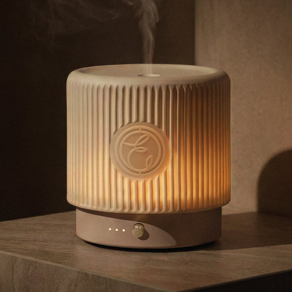 A beige humidifier emitting steam on a wooden surface with a dark background
