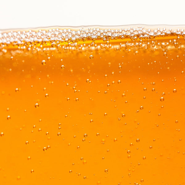 Close-up of a glass filled with orange liquid, likely beer, with bubbles on a white background.