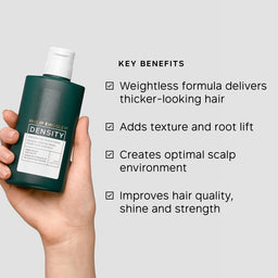 Hand holding a bottle of Philip Kingsley Density product with key benefits listed on a gray background