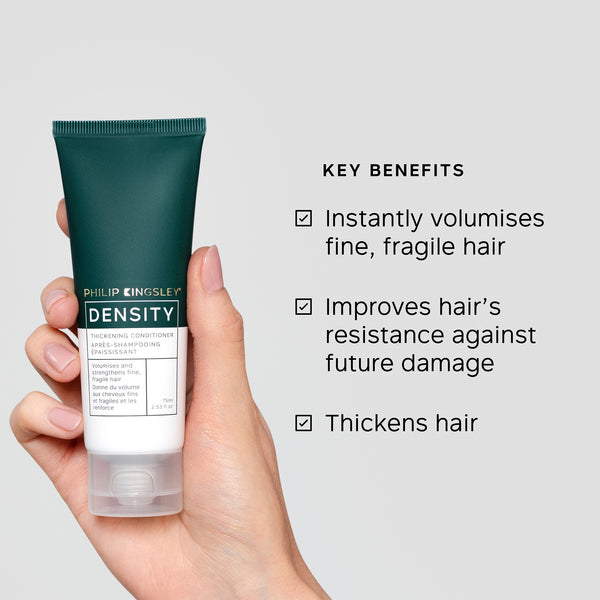 Hand holding a tube of Philip Kingsley Density conditioner with key benefits listed on a gray background