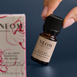 NEOM essential oil bottle held by a hand with a NEOM box in the background