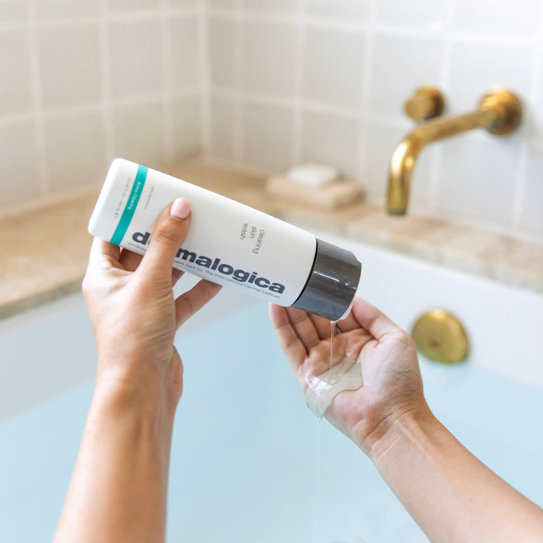 Person holding a bottle of Dermalogica product over a bathtub.
