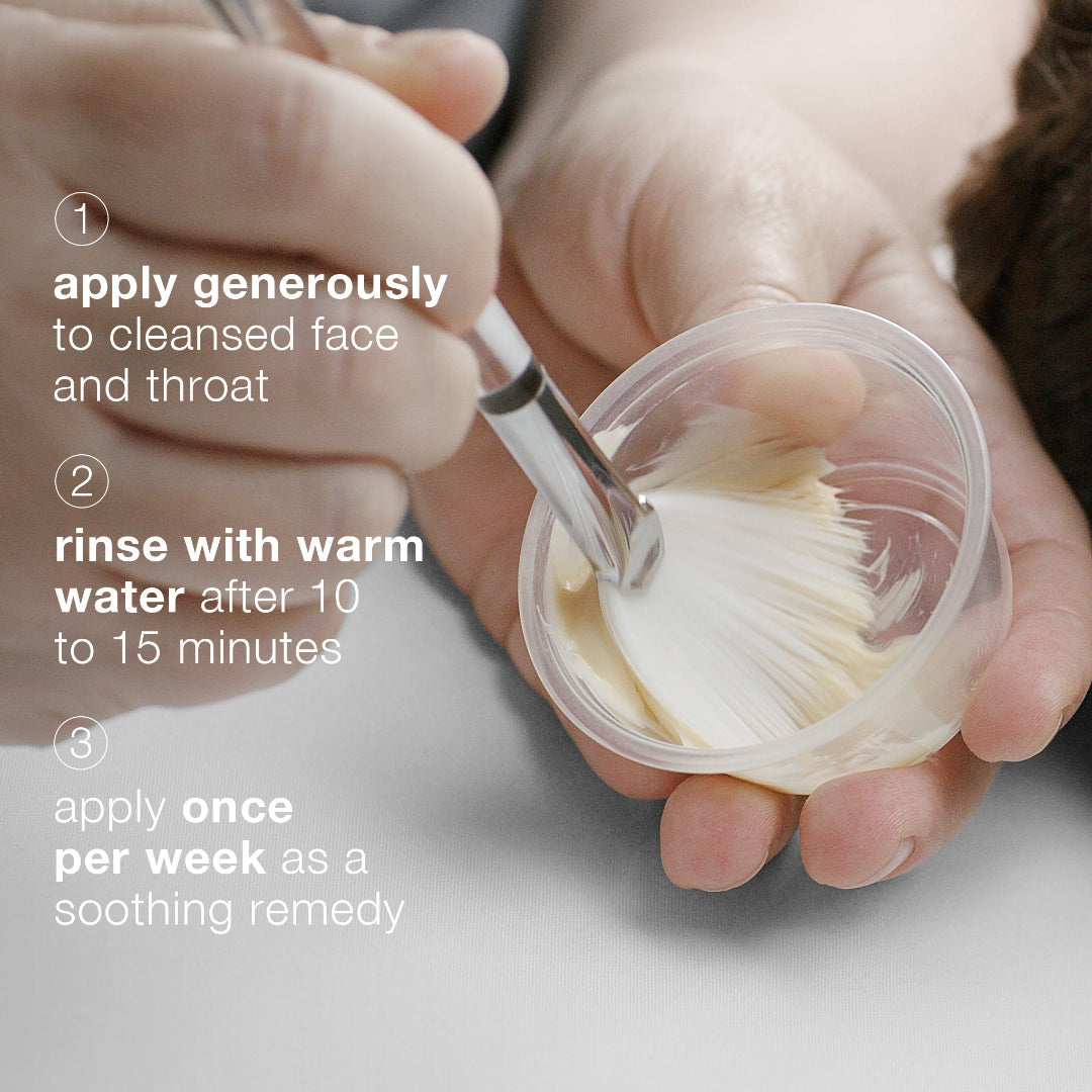 Person holding a container with a brush, applying a product to their face.