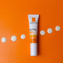 La Roche-Posay sunscreen tube on an orange background with white dots.
