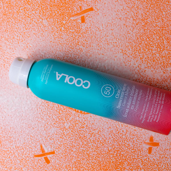 Coola sunscreen spray bottle on an orange textured background