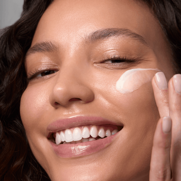Woman applying cream to her face with a neutral background