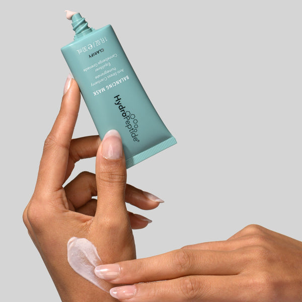 Hand applying a skincare product from a tube labeled 'hydropeel' on a gray background
