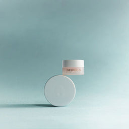 A small cosmetic jar with a white lid floating above a matching round white container on a soft blue gradient background. The jar label shows the brand name UNIBOYA.