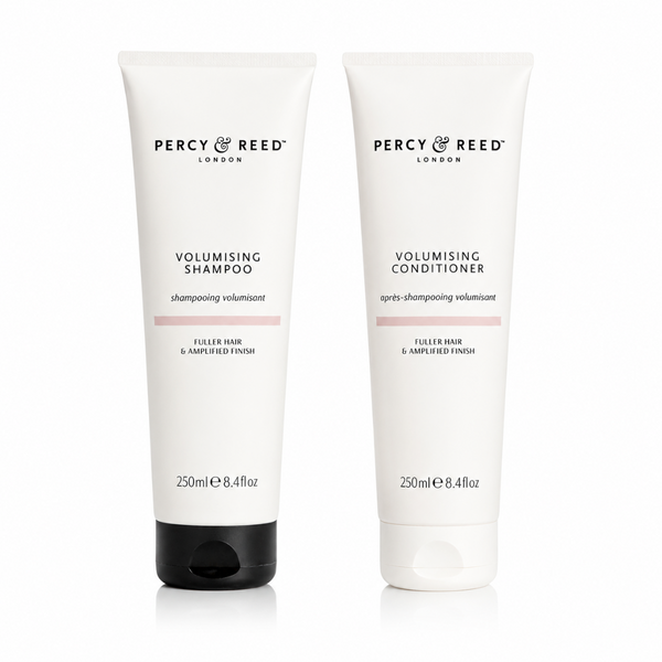 Two white tubes of Percy Reed London Volumising Shampoo and Volumising Conditioner side by side on a white background. The shampoo tube has a black cap, and both tubes feature black text and a thin pink accent line.