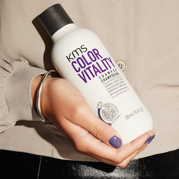 KMS Color Vitality shampoo bottle held in a hand against a neutral background