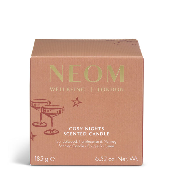 A square cardboard box for a scented candle by NEOM, featuring a dusty rose pink color with gold lettering and small gold star illustrations. The text reads 'NEOM WELLBEING | LONDON' and 'COSY NIGHTS SCENTED CANDLE'.
