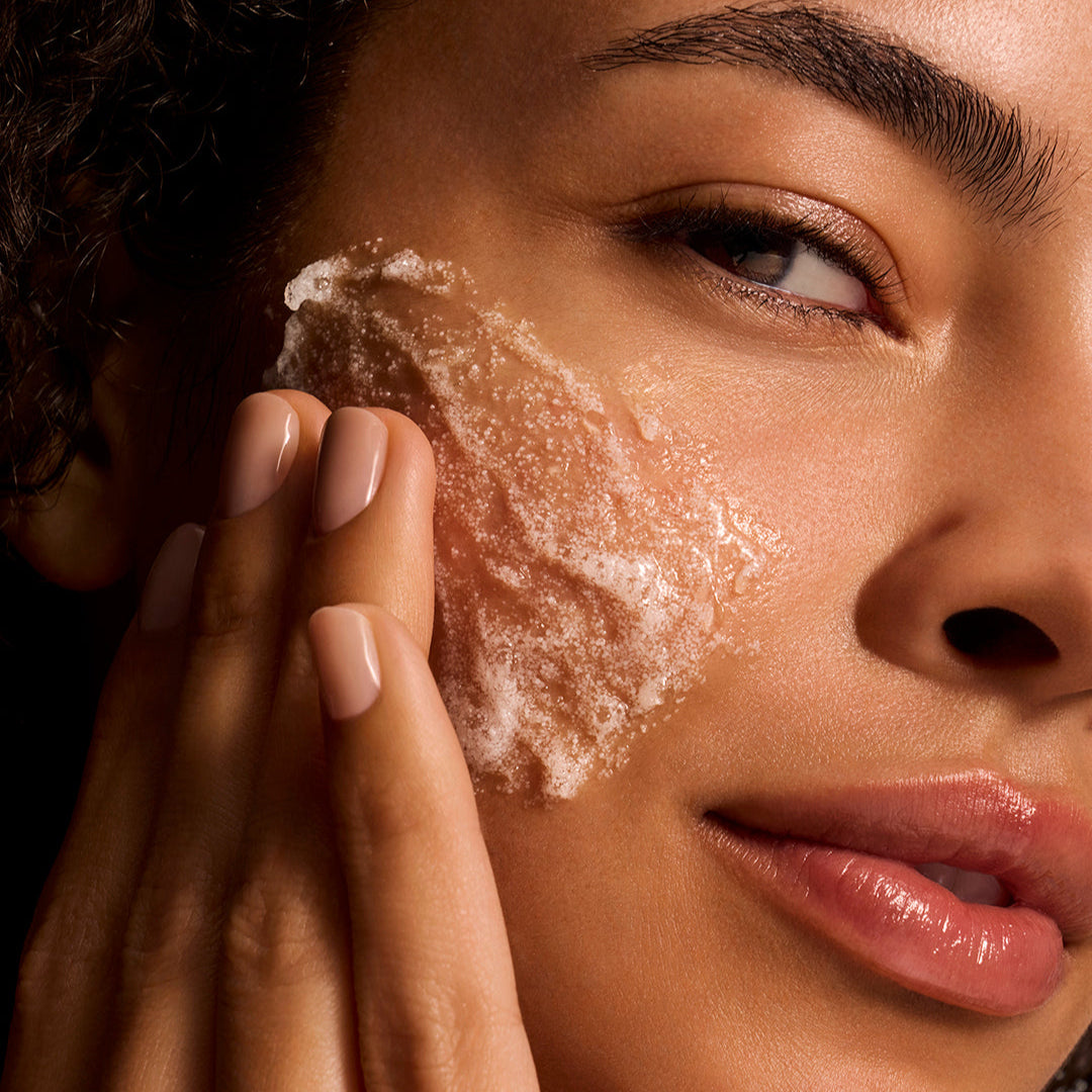 Close-up of a person applying a facial scrub to their cheek.