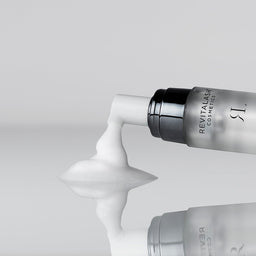 Revitalash cosmetic bottle with white cream being squeezed out on a light gray background
