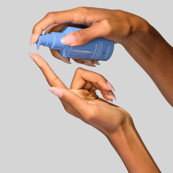 Hand applying a blue skincare product to another hand against a gray background