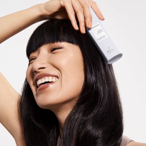 Woman with long black hair holding a bottle of hair product against a white background