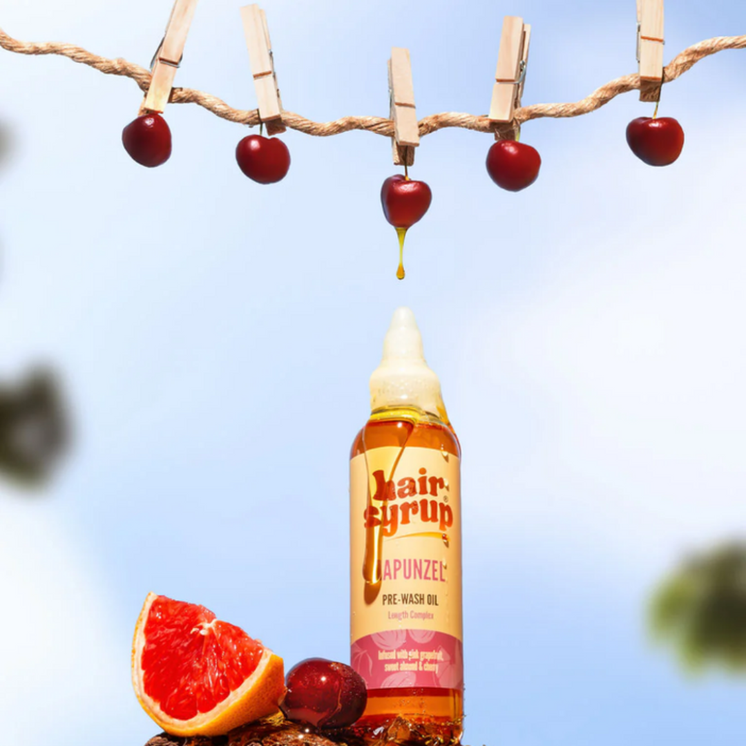 Bottle of Hair Fyrn Apunzel Pre-Wash Oil with grapefruit and cherries on a clothesline against a blue sky.