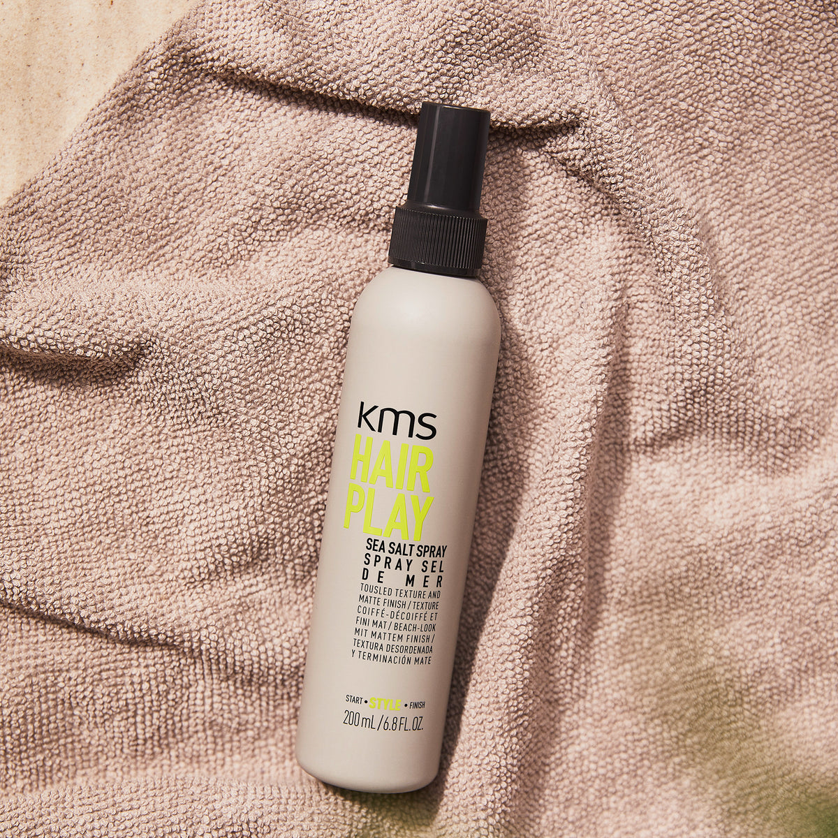 KMS Hair Play sea salt spray bottle on a textured surface