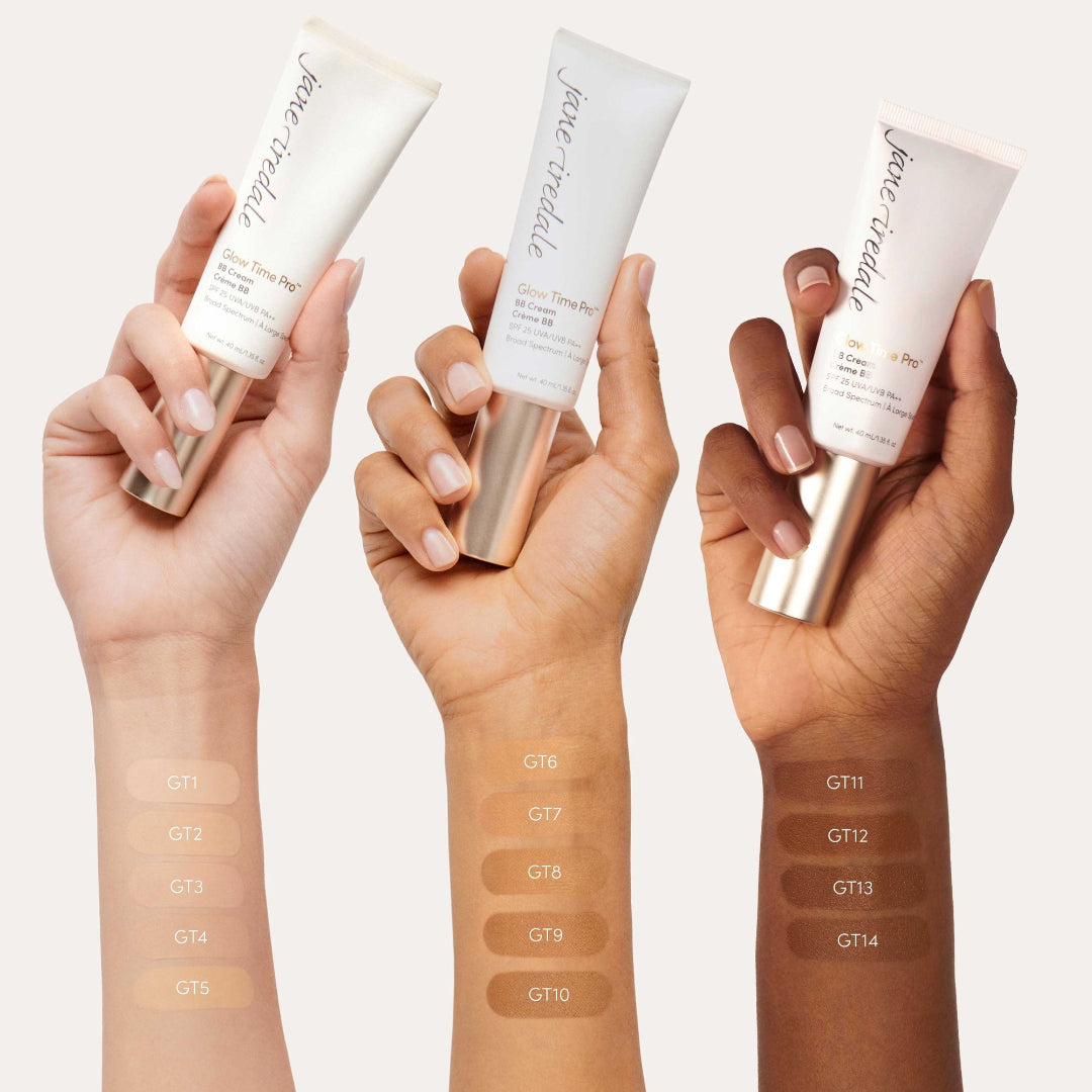 Three hands holding Jane Iredale foundation tubes with color swatches on a white background