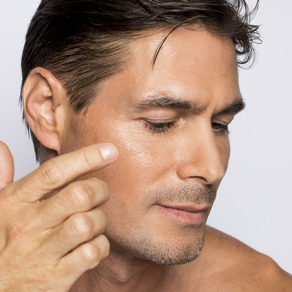 Man applying cream to his face with a neutral background