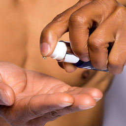 Person applying a small amount of liquid from a bottle onto their palm.