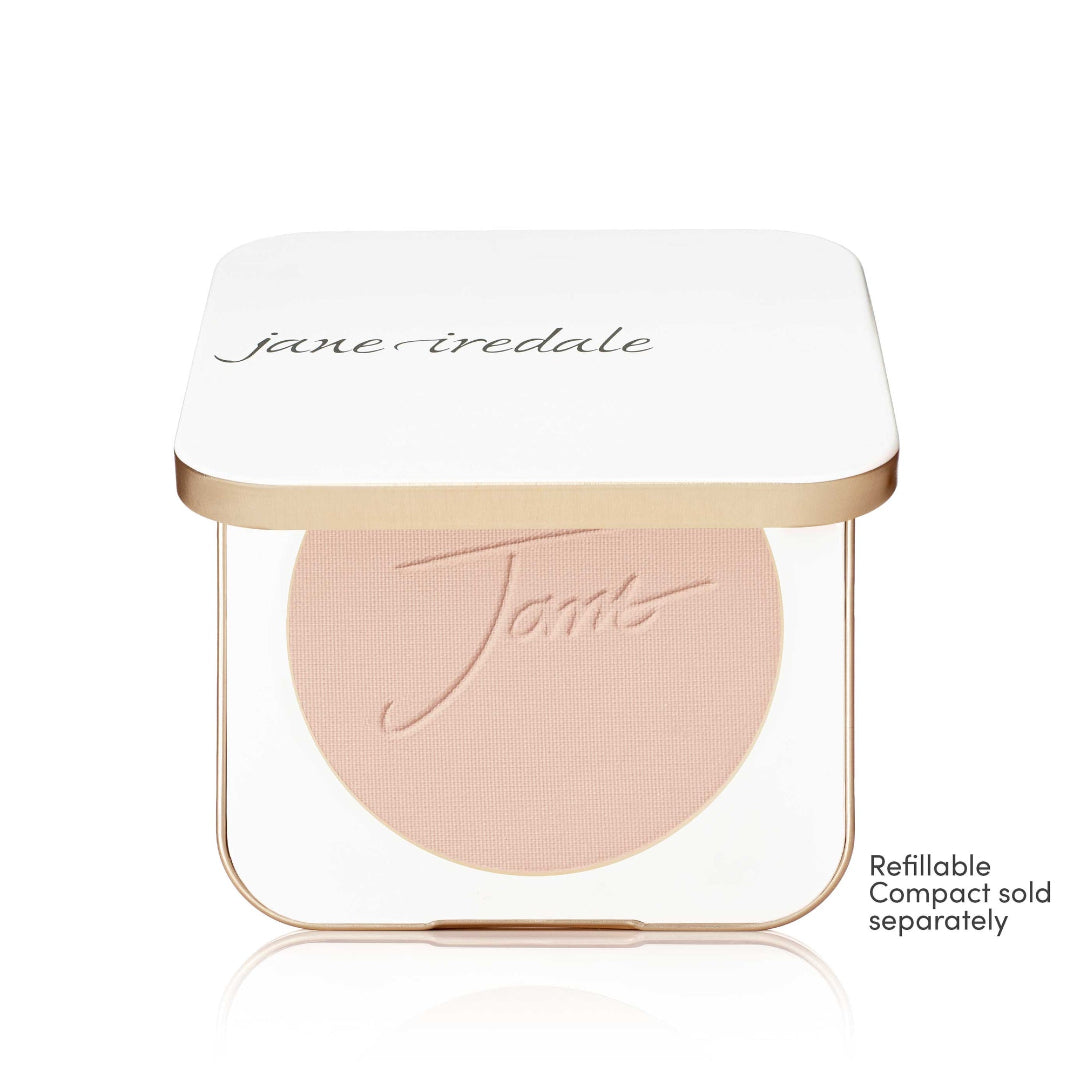 A Jane Iredale makeup compact with a white lid and a clear base showing a round blush or pressed powder in a light peach-beige shade. The compact has a thin metallic gold frame.