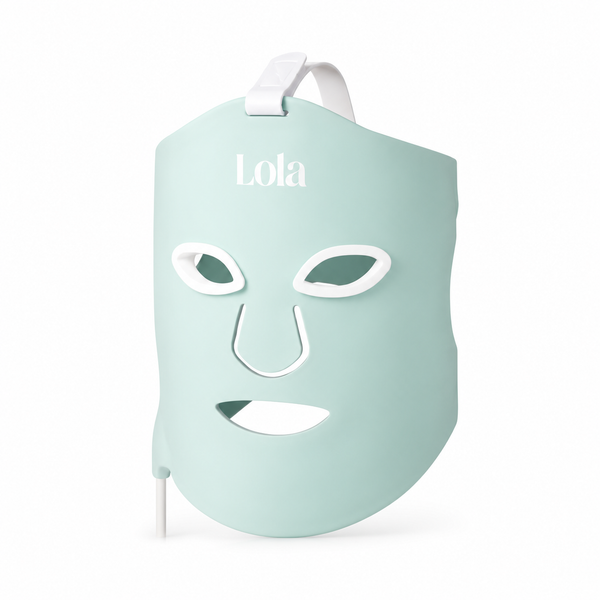 A light mint green LED facial therapy mask with white cutouts for the eyes, nose, and mouth, featuring a white strap at the top and the brand name 'Lola' printed in white on the forehead, set against a plain white background.