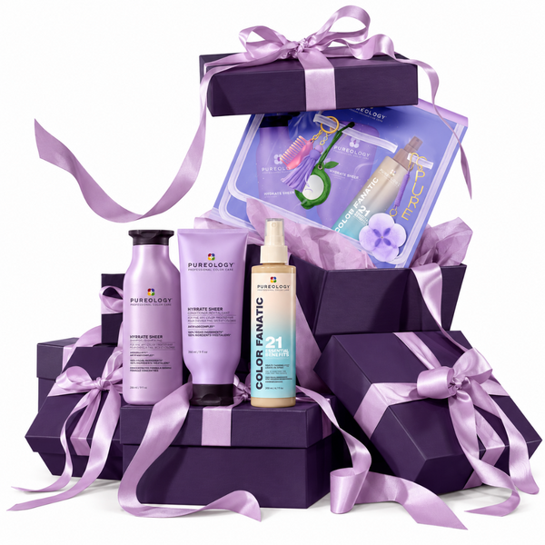 A haircare gift set arranged in stacked purple gift boxes with lavender satin ribbons on a white background. Visible products include Pureology Advanced Biotin Shampoo, Advanced Breaker, Color Fanatic 1-4 Color Protect Spray, and a purple hair color treatment kit booklet.