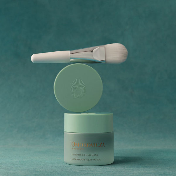 A jar of One De Vica Extraordinary Nail Mask with a matching brush and lid, displayed on a textured teal background.